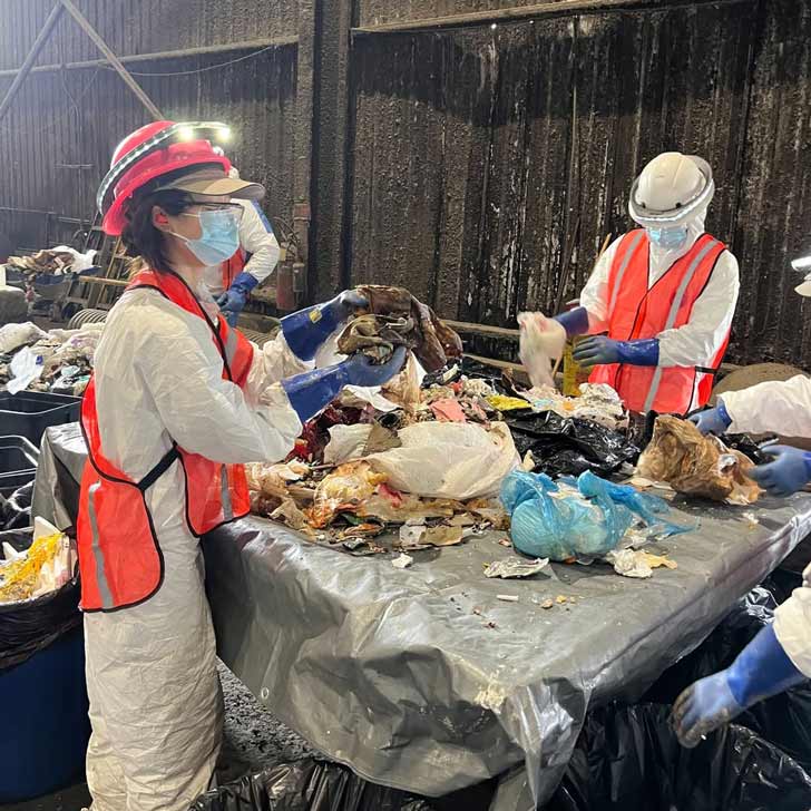Two people sort through trash in a waste facility in New York