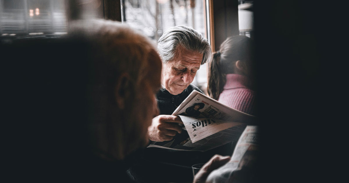 An elderly man reads a newspaper in a crowded cafe