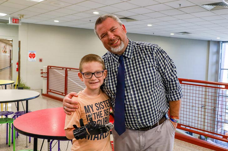 A teacher smiles with a student who has a 3D printed prosthetic hand