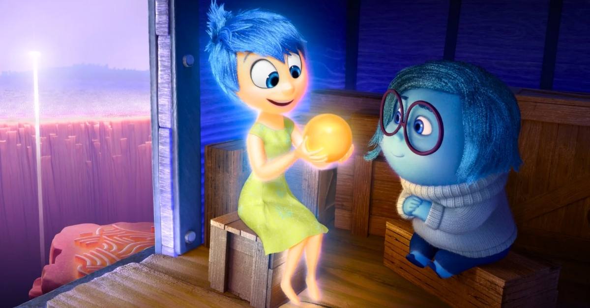 A still from the movie "Inside Out" in which a blue haired yellow emotion named Joy holds up a golden glowing memory to their friend Sadness, a blue emotion.