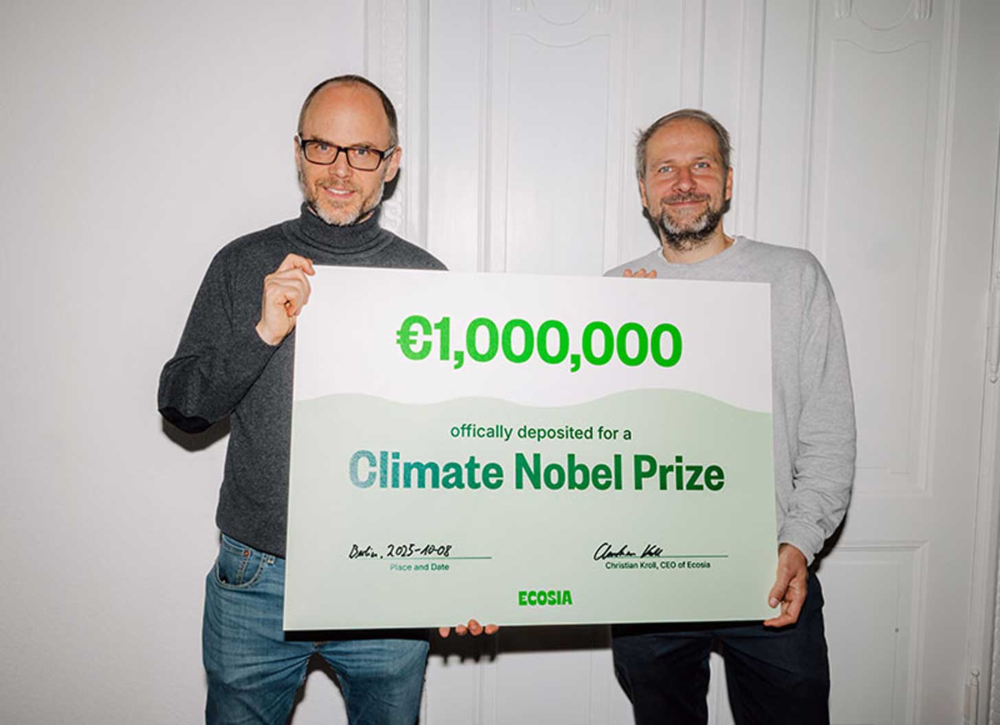 Two men, the founders of Ecosia, hold up a large check for €1 million, designated for a Climate Nobel Prize