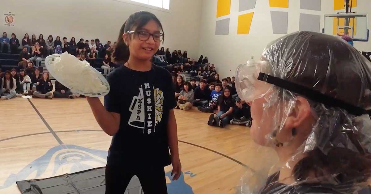 A middle schooler throws a pie in the face of her teacher at a school assembly