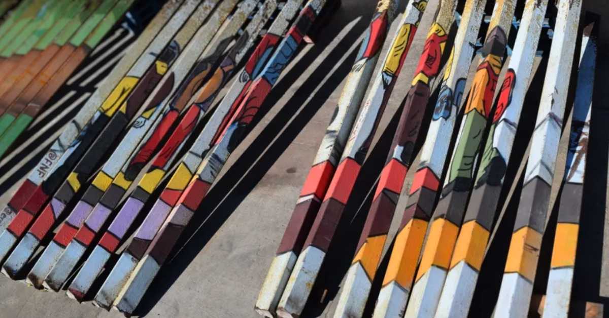 Slats of a wall covered in paint depicting migrants crossing