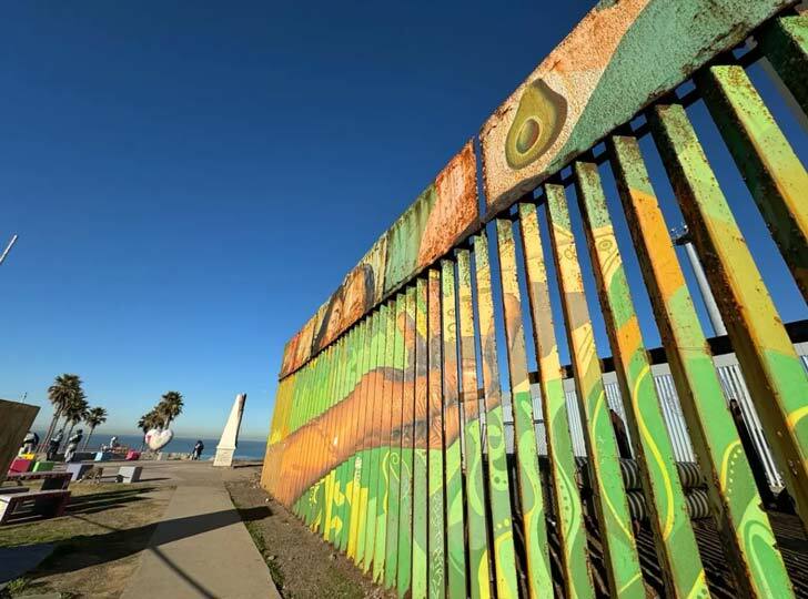 Colorful green paint across tall metal slats at the U.S. and Mexico border