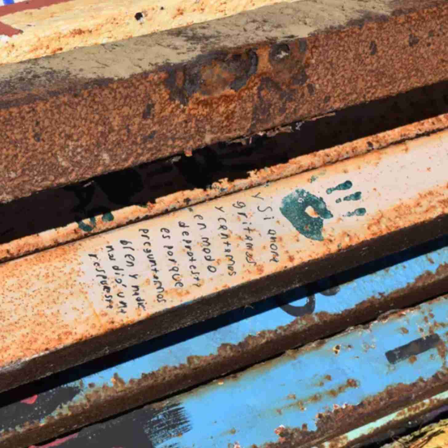 on the slats of the U.S. Mexico border wall that was torn down is a painted hand and a message in Spanish