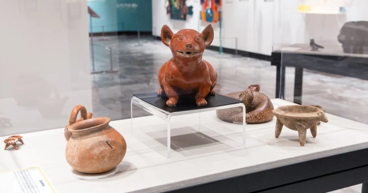 A statue of a Mexican dog rests besides tiny pots and clay artifacts.