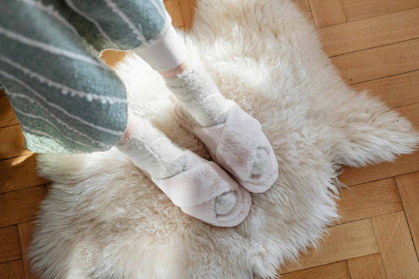 A person wears pastel pink slippers with gray fuzzy socks underneath