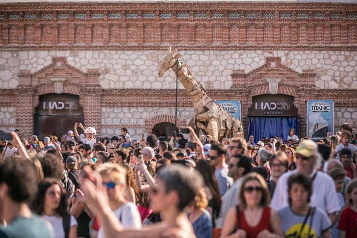 A large cardboard giraffe puppet overlooks a crowd of people in Madrid, Spain