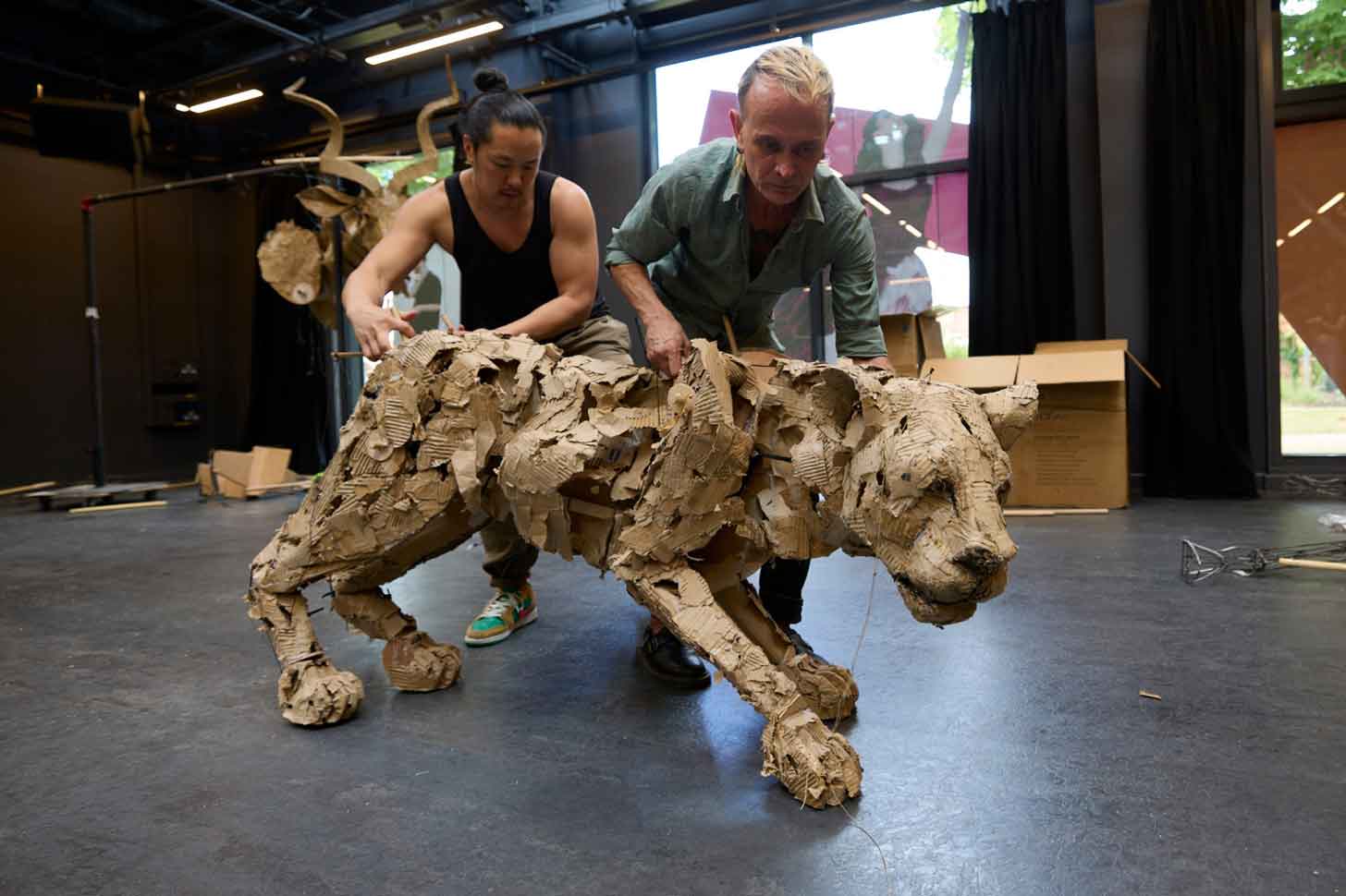 Two puppeteers create a life-size lion puppet out of cardboard and recycled materials