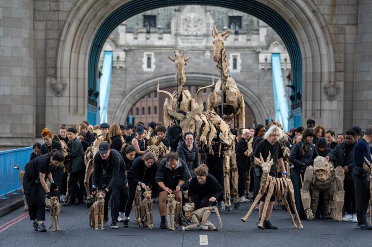 A herd of puppeteers with cardboard, life-size animals crosses Tower Bridge in London