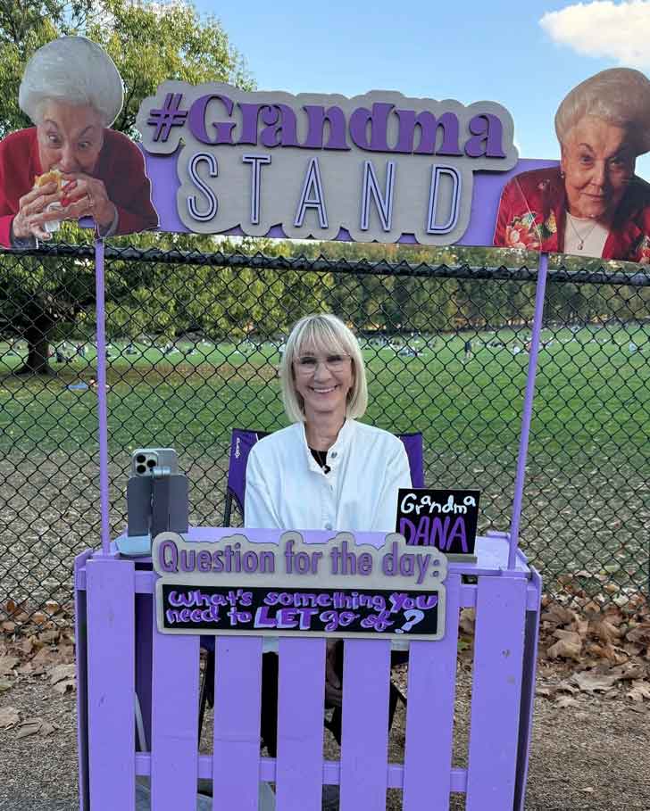 An old woman sits at a purple lemonade stand in Central Park called The Grandma Stand