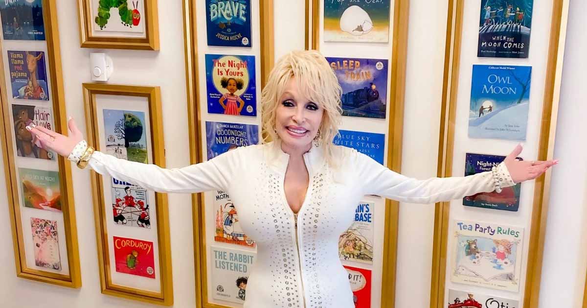 Dolly Parton stands in front of a wall of children's books with her arms outstretched