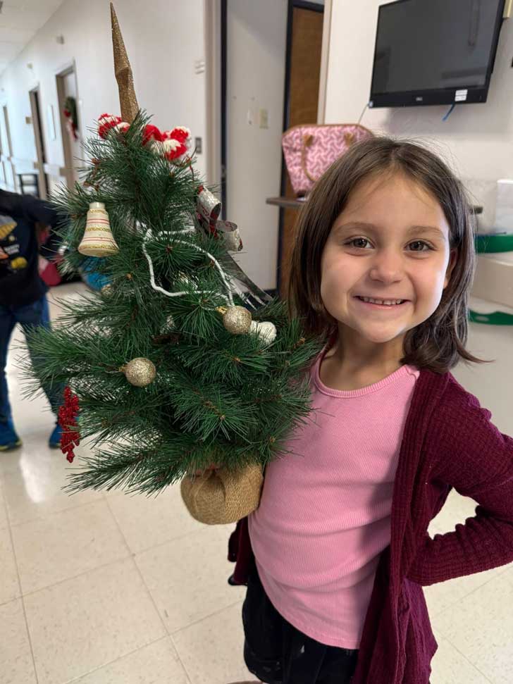 A young girl holds up a small Christmas tree in a nursing home