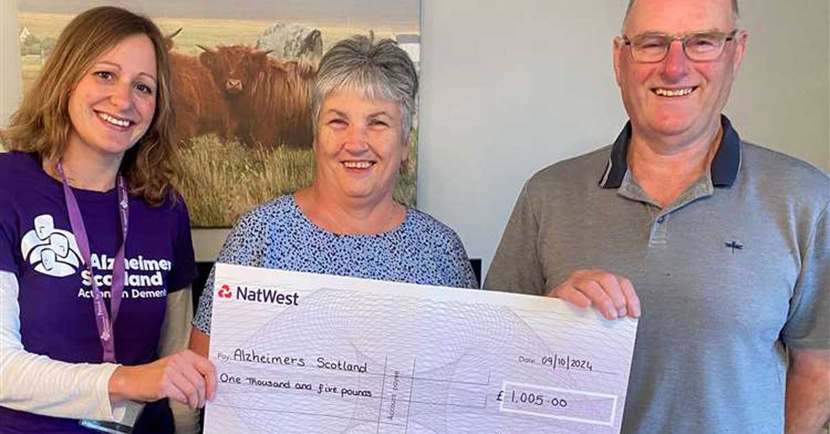 A couple holds a large check with a leader of Alzheimer Scotland