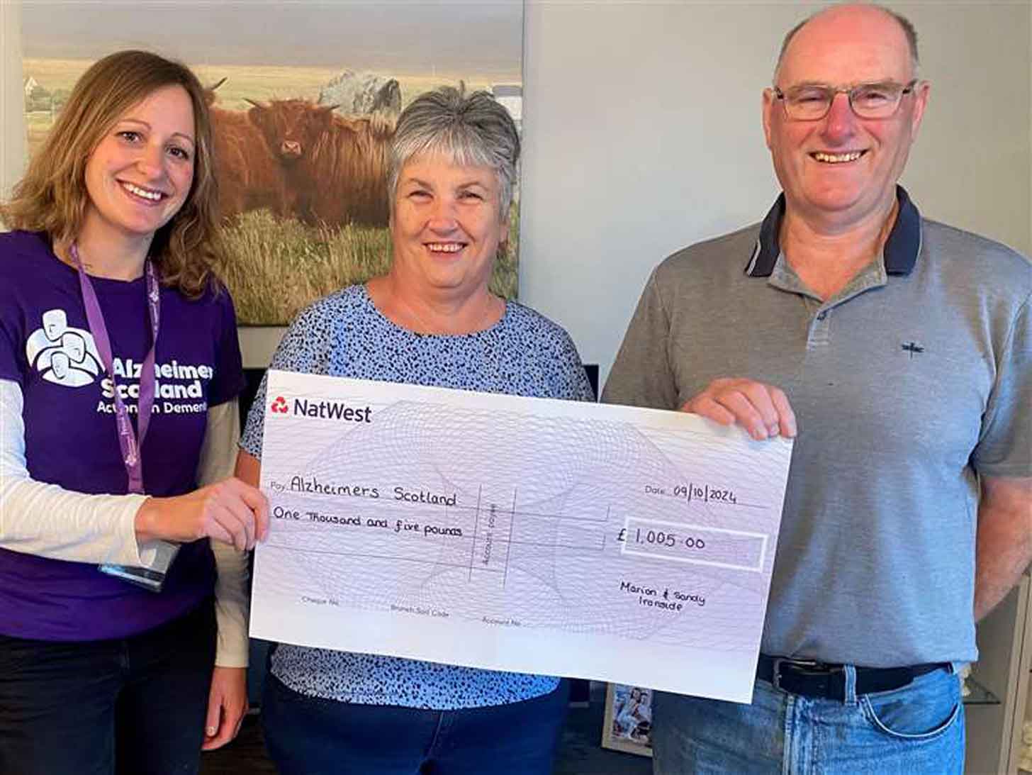 A couple holds a large check with a leader of Alzheimer Scotland