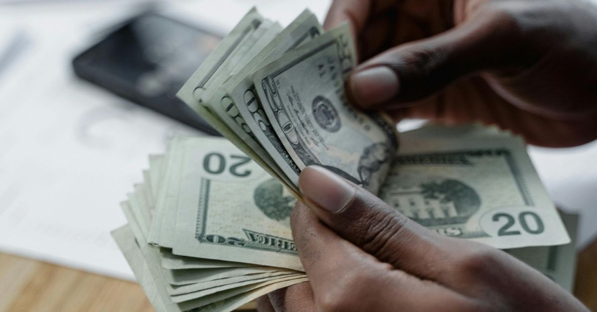 A close-up of hands leafing through a stack of twenty dollar bills