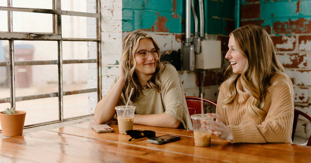 Two women sit in a cafe talking over iced lattes
