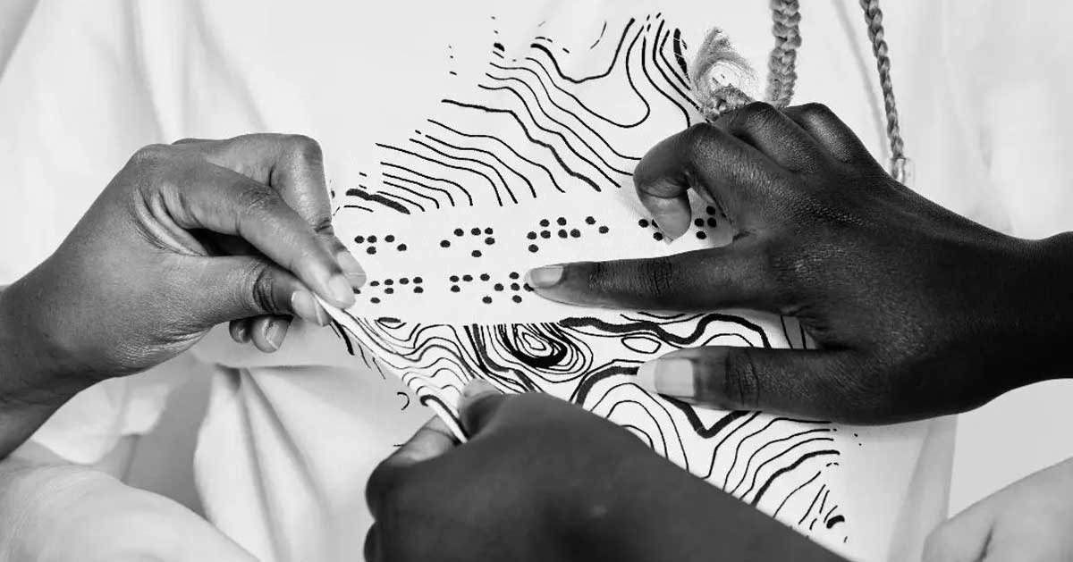 Hands touch a graphic T-shirt to read words in Braille