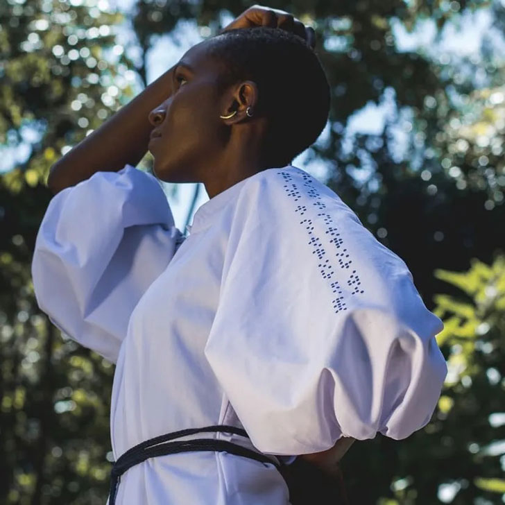 A woman wears a white puff-sleeve dress with Braille letters on the arms