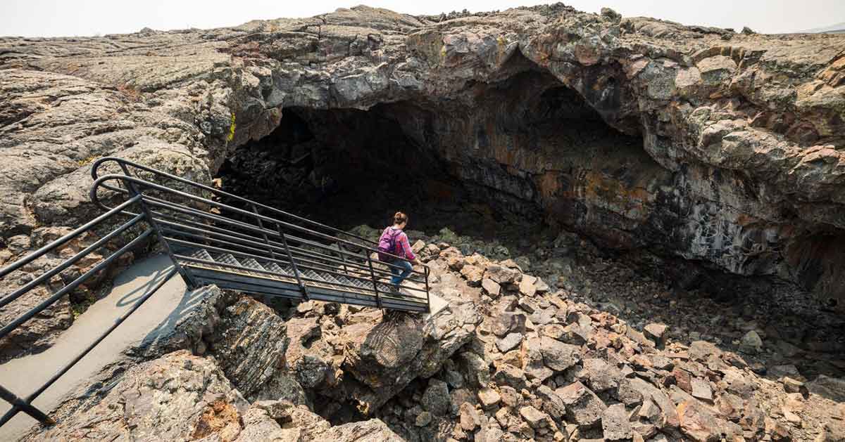 A person walks down a flight of stairs into a cave at Craters of the Moon National Monument