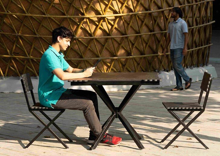 The Hungry Caterpillar -- a bamboo structure winding around kitchen stalls printed from concrete. In this shot, a student sits at a table and smiles at his phone as another student walks in the background