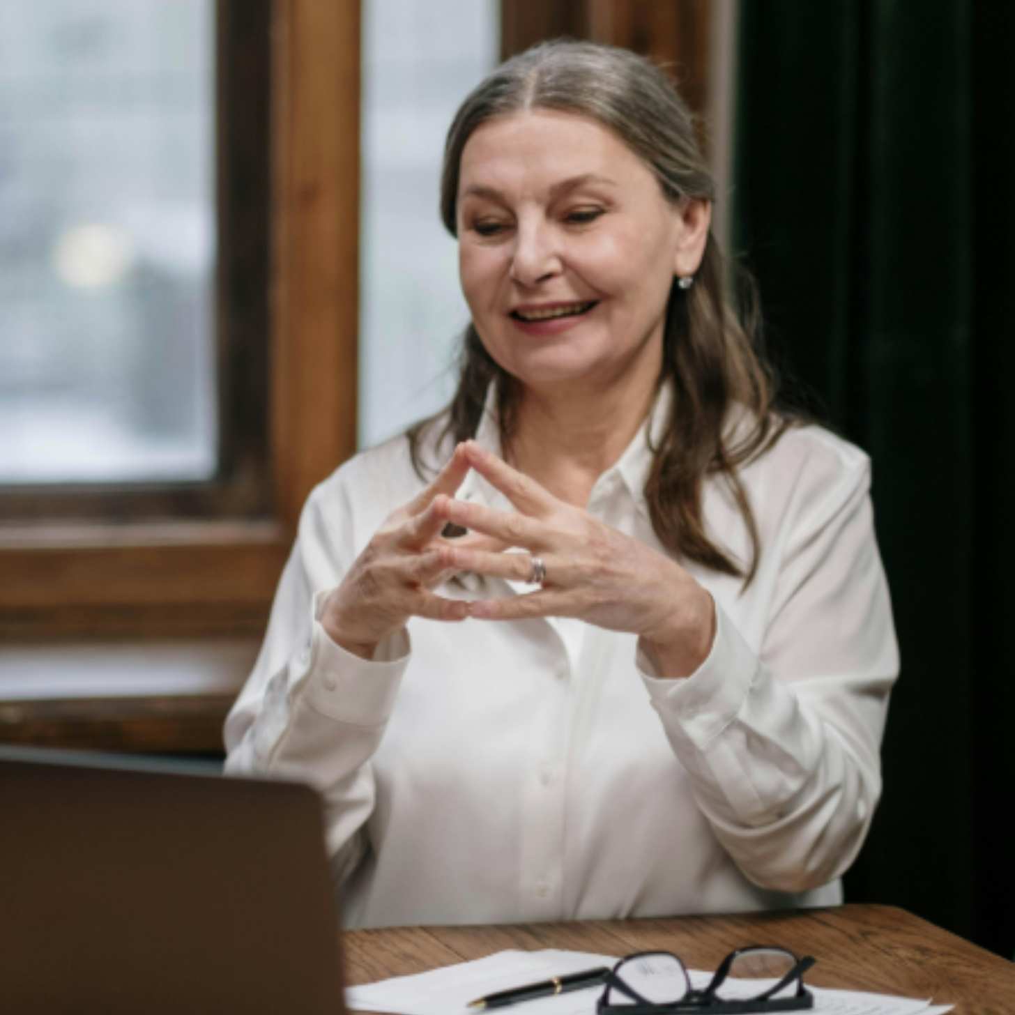 An older woman, perhaps in her 60s or 70s, is talking while looking at a computer, presumably on a video work call
