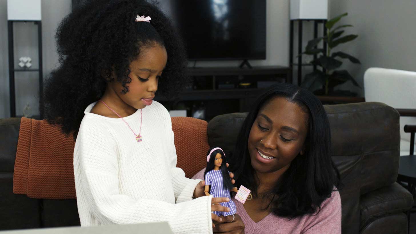 A Black mom and daughter play with an autistic Barbie doll