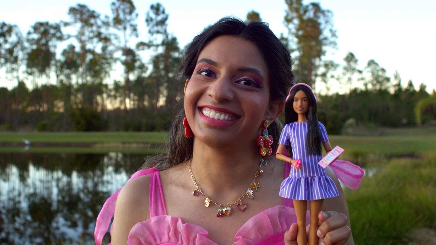 Fashion designer Aarushi Pratap stands outside, holding up an autistic Barbie doll, smiling