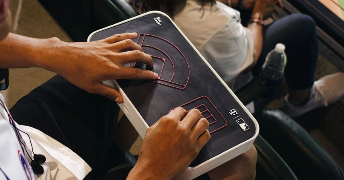 A sports fan uses a haptic feedback device while sitting in the stands of a baseball game.