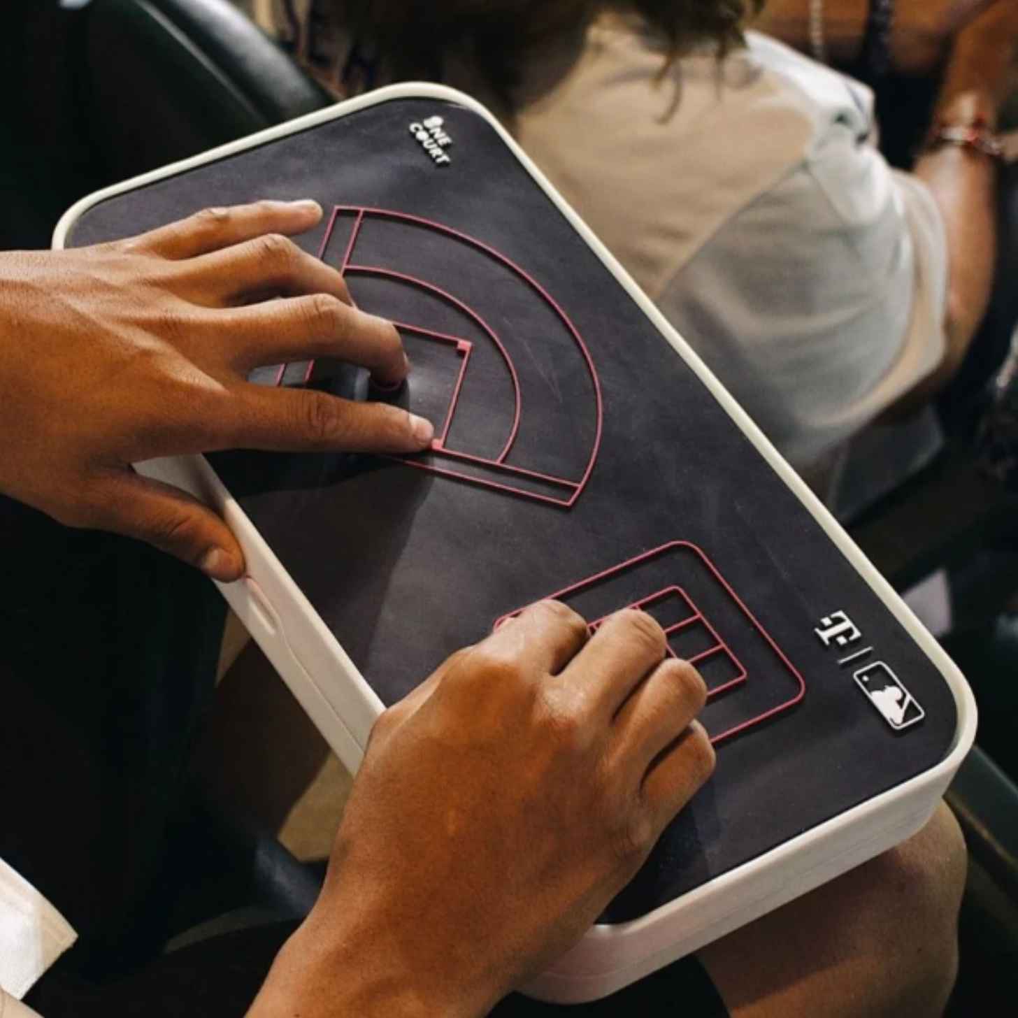 A sports fan uses a haptic feedback device while sitting in the stands of a baseball game.