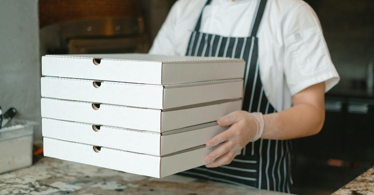 A person holds four white takeout pizza boxes
