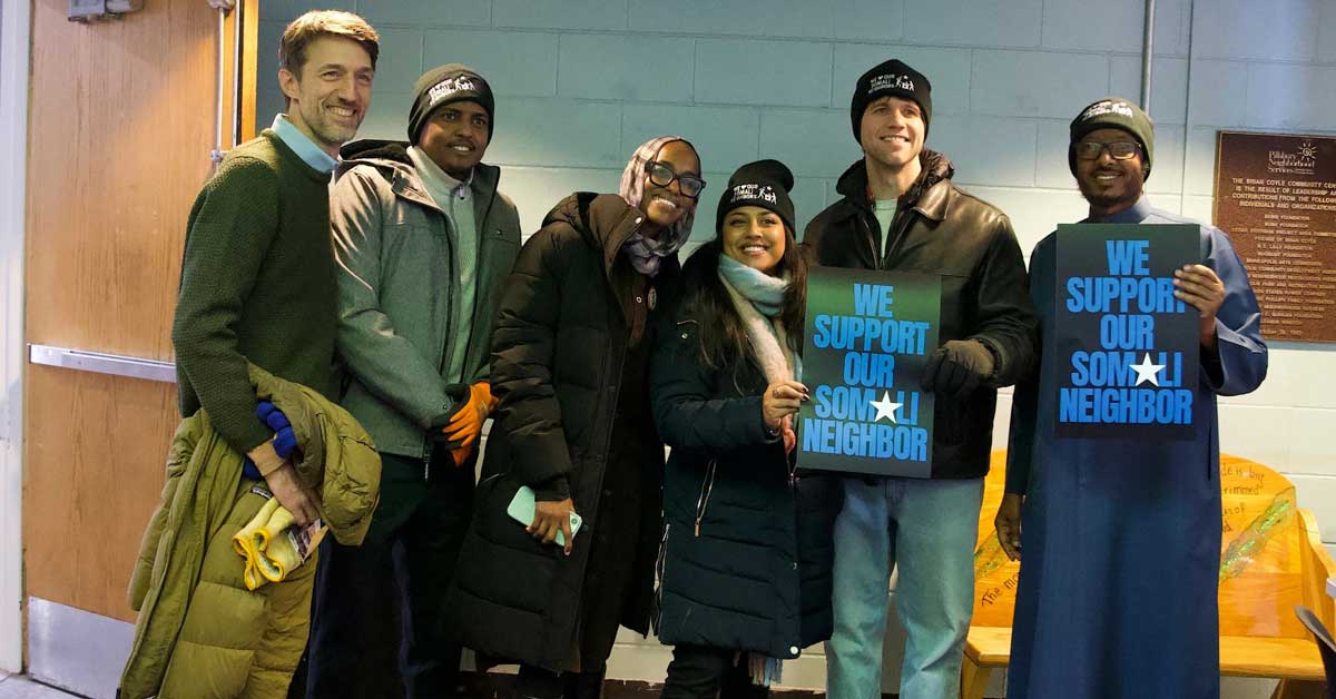 A group of people, both Somali and allies, pose for a group photo in Minnesota, holding up signs that read: "We support our Somali neighbor"