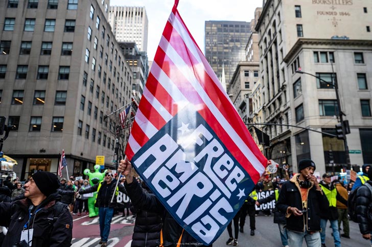 A person waves a flag in a protest that says "Free America"