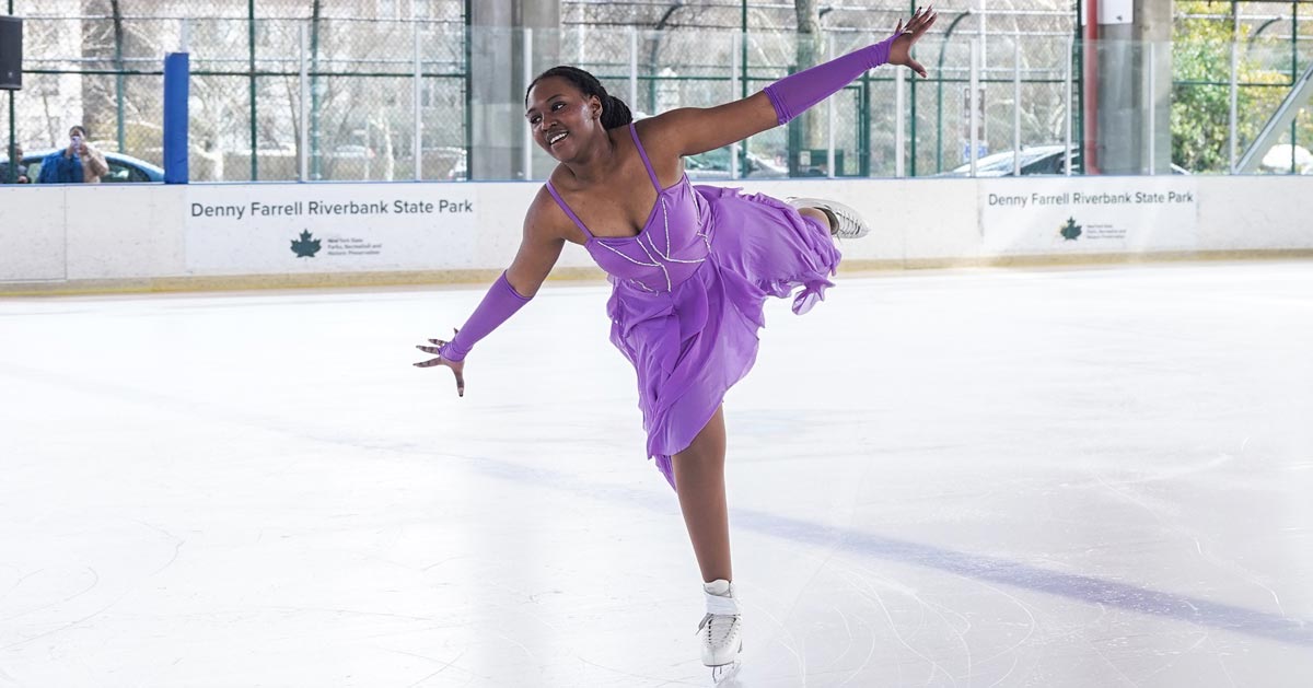 A young Black woman in a purple dress ice-skates in a rink