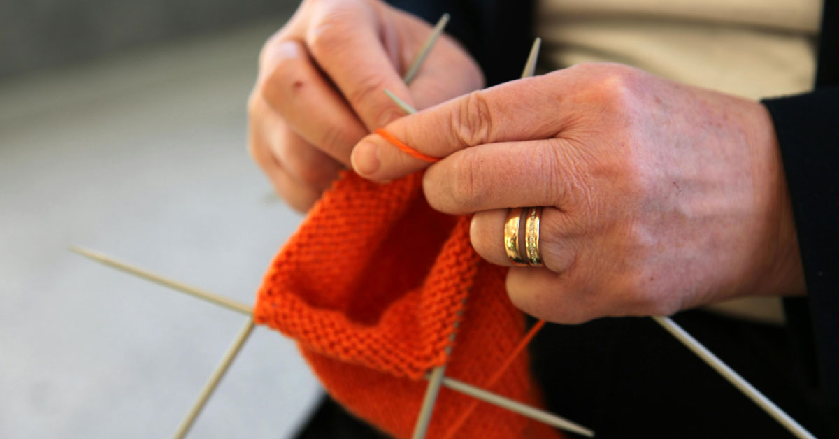 A close-up of a person knitting a red hat