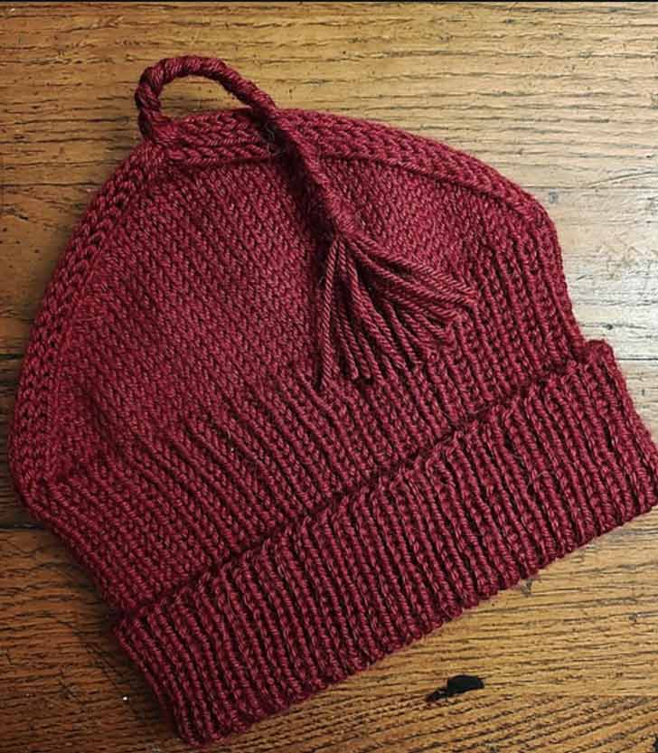 A red knitted beanie with a tassel sits on a wooden countertop