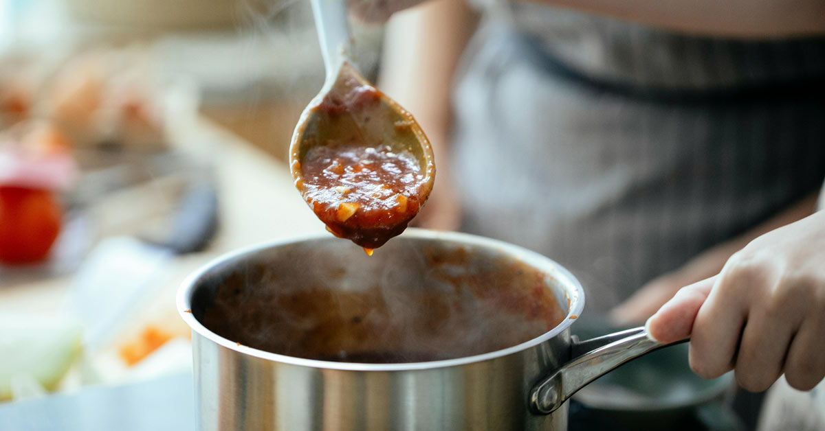 A close-up of a spoonful of sauce cooking over a simmering pot