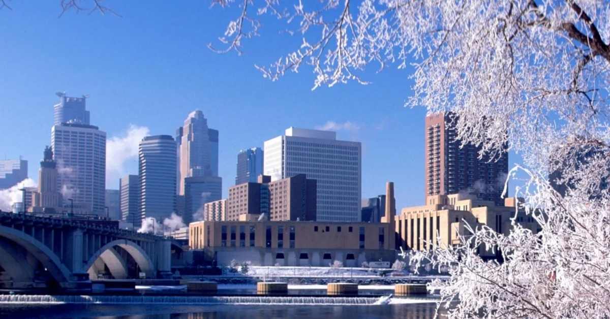 The city of Minneapolis as seen from a distance, framed by snow covered trees. 