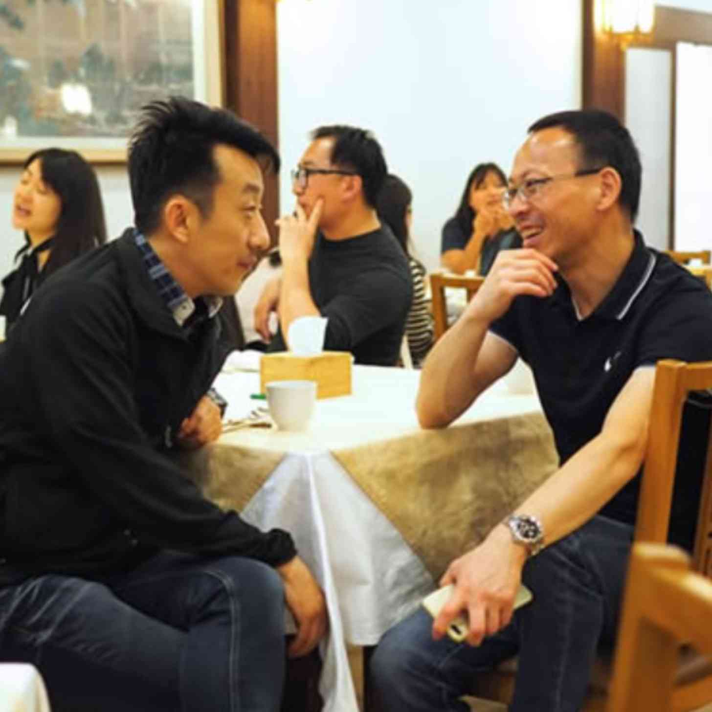 Two Korean men smile as they talk to each other in a classroom setting