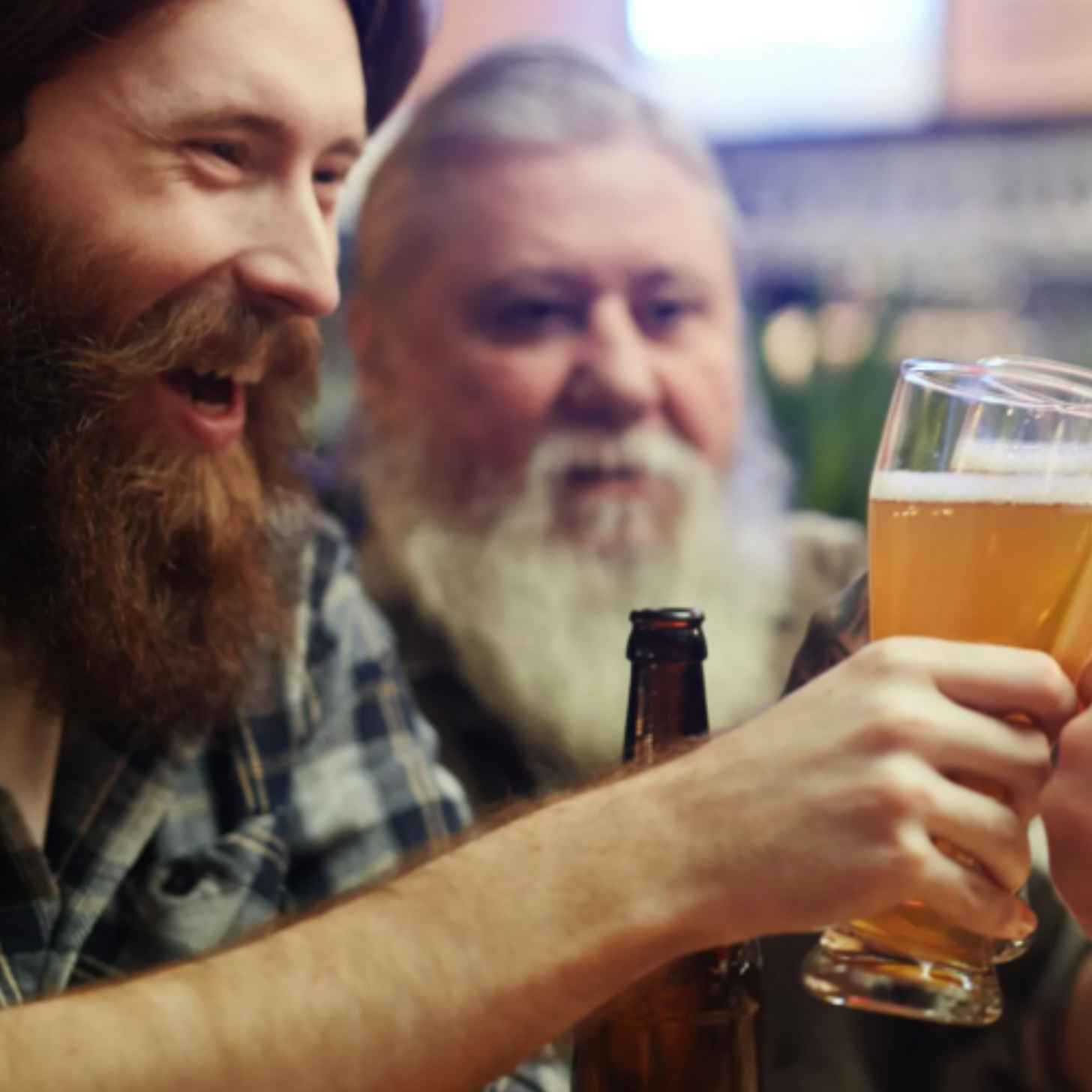 A group of men smile as they cheers beers together in a bar.