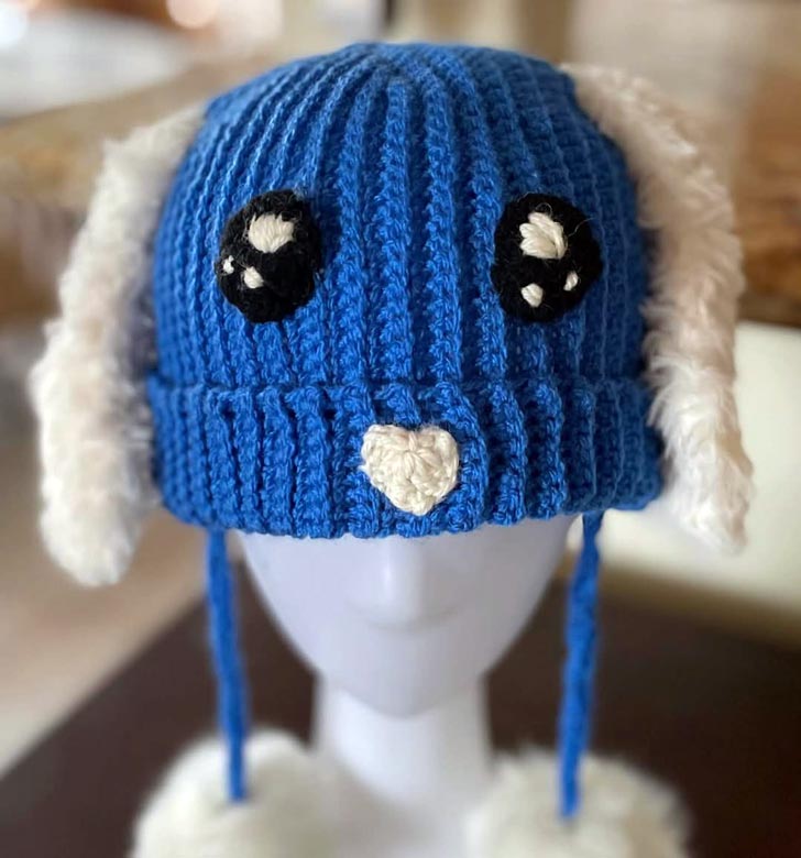 A blue crocheted winter hat with eyes and white bunny ears on a mannequin