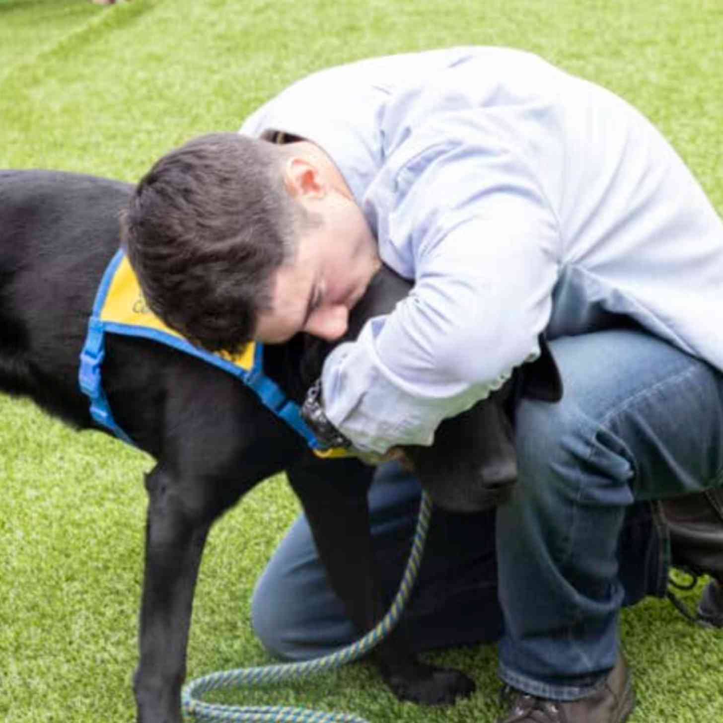 A young man in a prison uniform embraces a black lab.