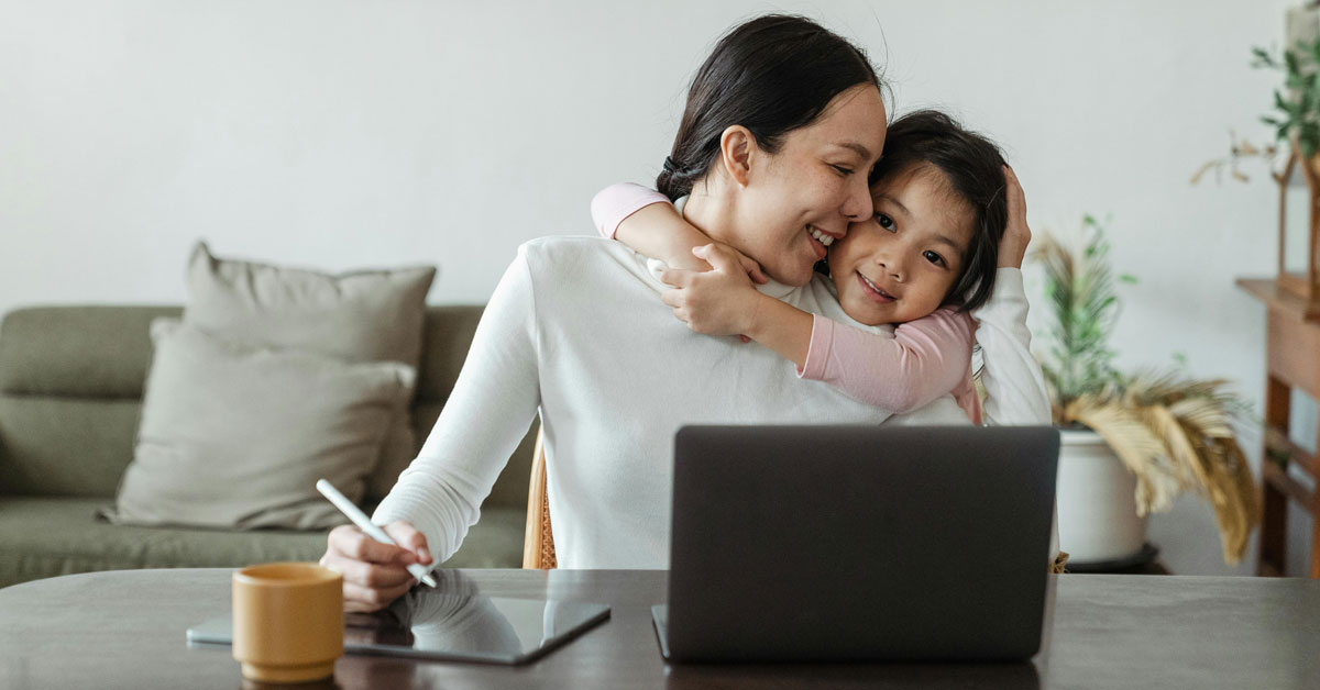 A mother and daughter snuggled up at home, behind a laptop