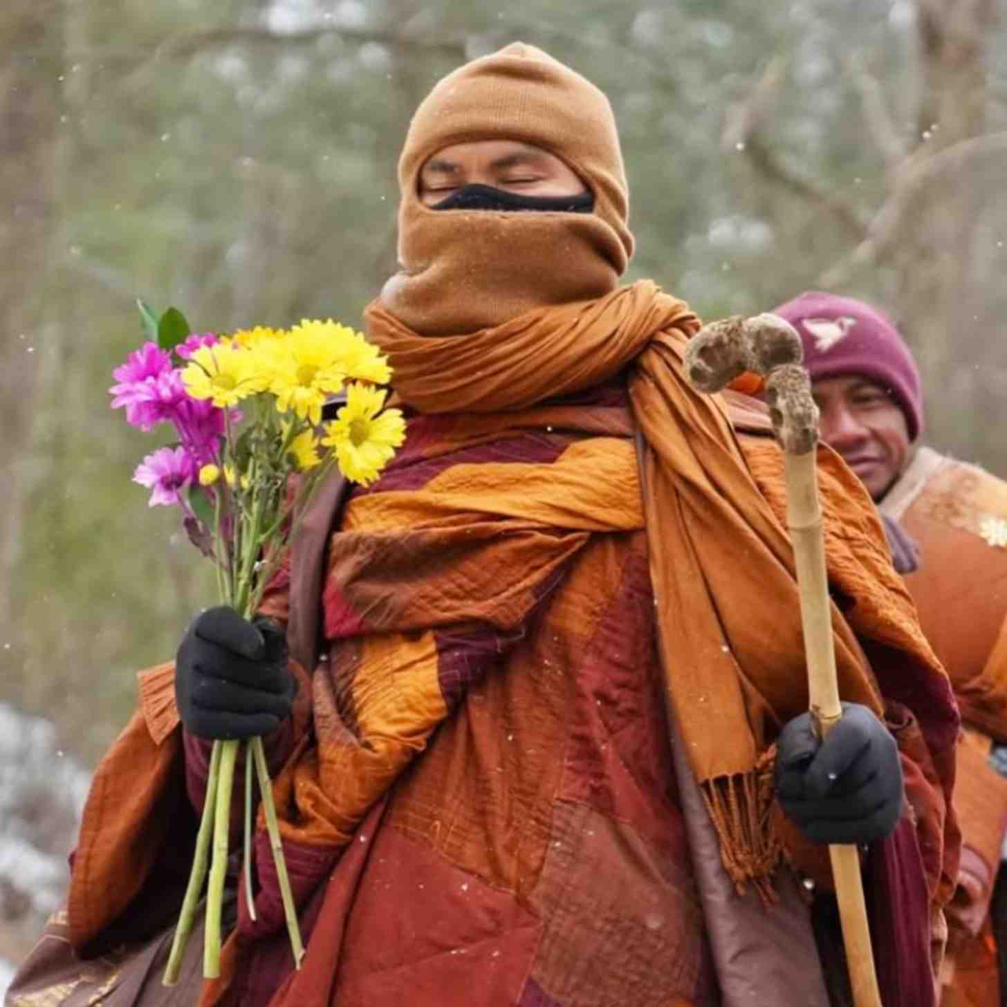A Buddhist monk closes his eyes as he prays, holding pink and yellow flowers in his hand. it is snowing around him.