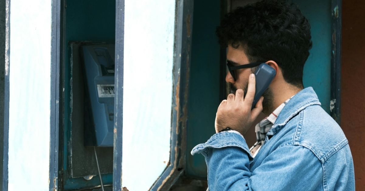 A man talks on the payphone at an old phone booth