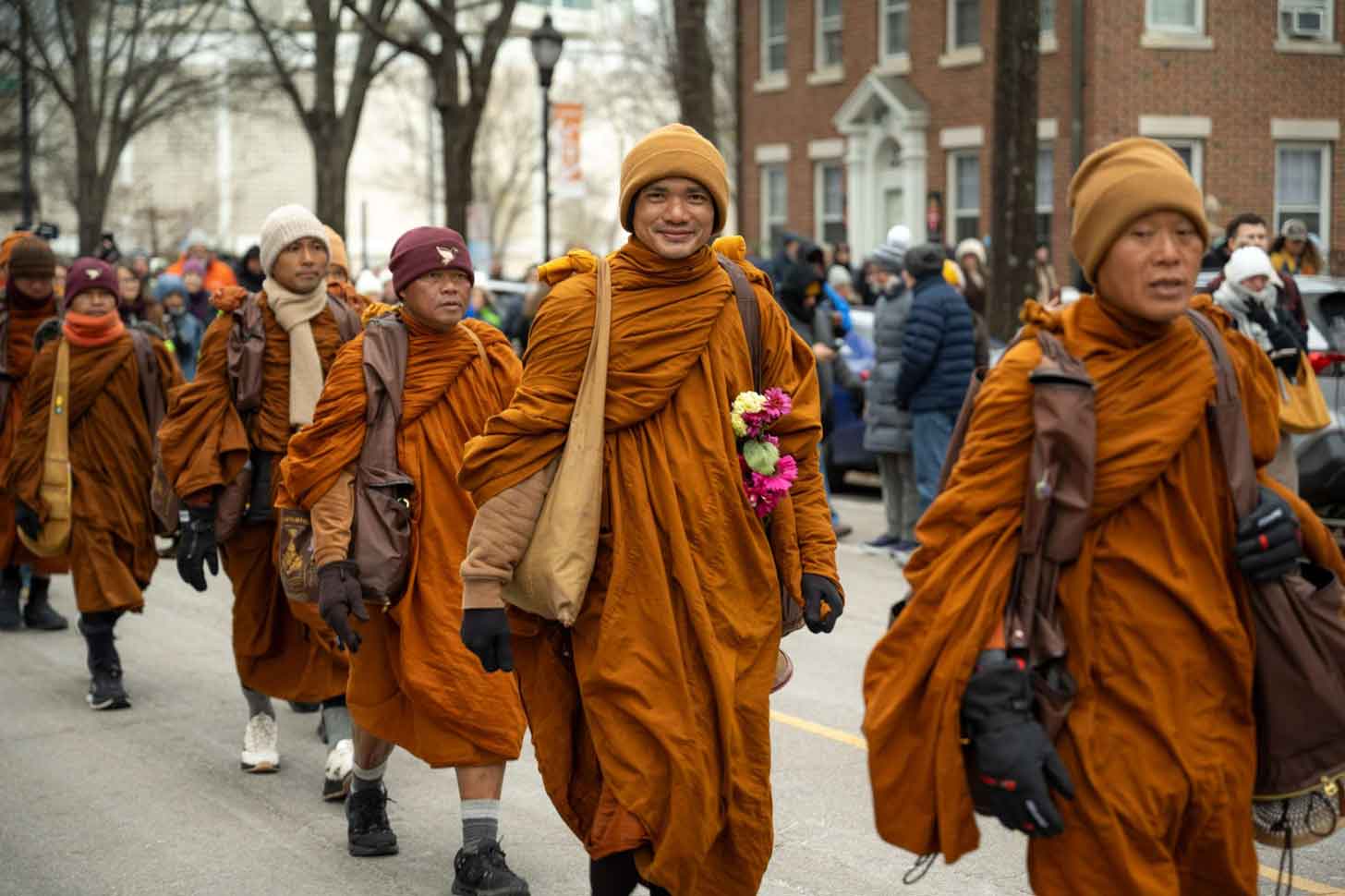A group of monks in orange robes walks down a crowded street, smiling