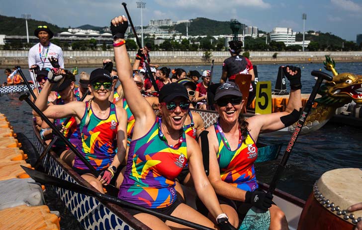 A dragonboat team smiles in the water, wearing rainbow pride jerseys at the 2022 Gay Games