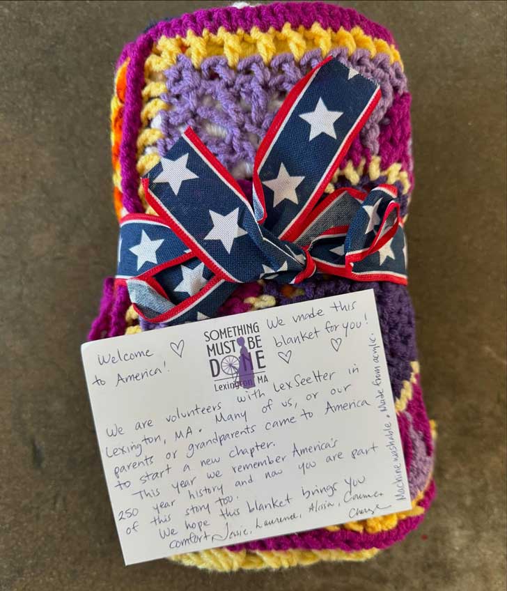 A handwritten notes is attached to a rolled blanket made with purple and yellow yarn is 