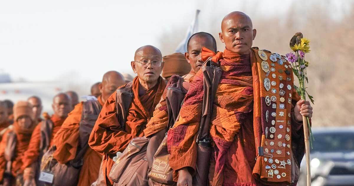 A group of Buddhist monks in orange robes walk down a street in their 2,300-mile walk for peace