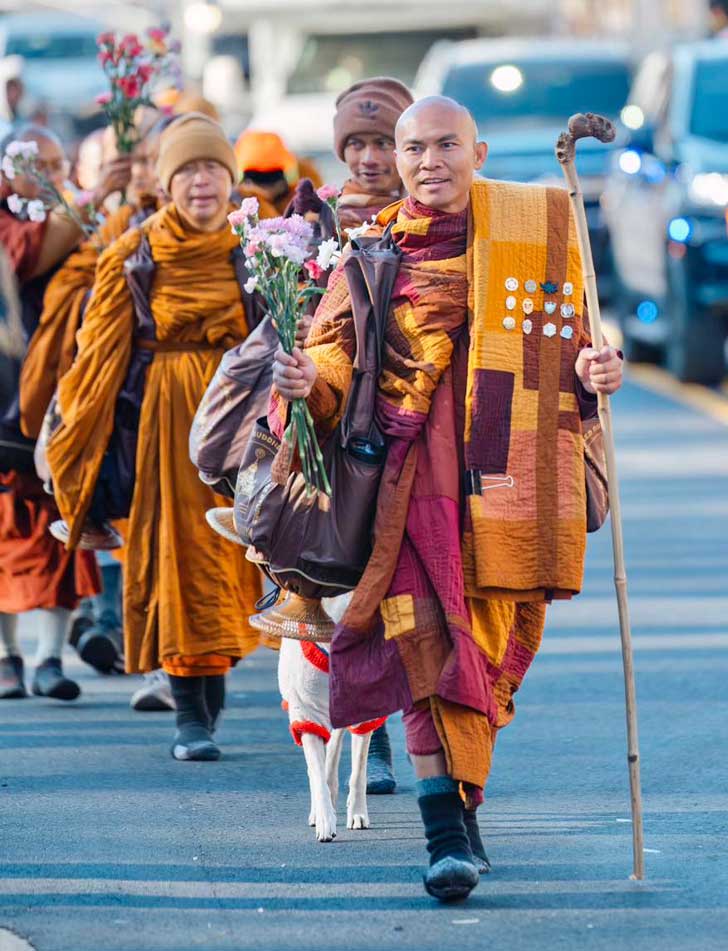 A group of Buddhist monks in orange robes carry flowers and walking sticks as they enter Washington, D.C.